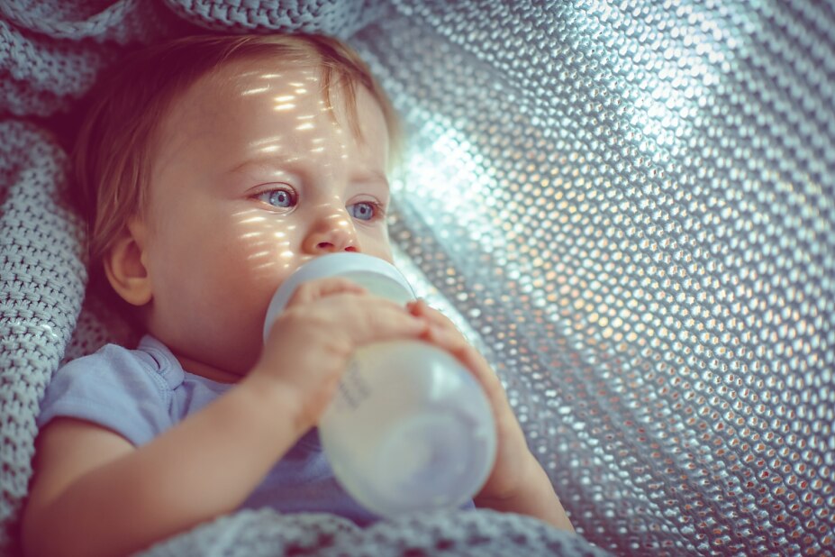 Baby liegt auf einer Decke und trinkt Milch aus einer Babyflasche.