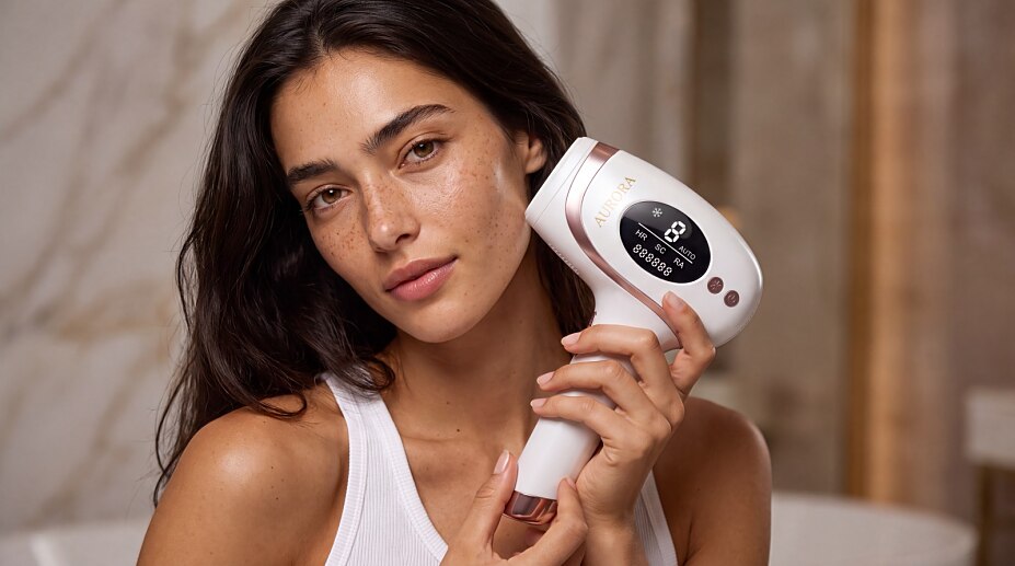 Frau hält das IPL Gerät Aurora PureSkin Ultra 9 im Badezimmer neben ihr Gesicht