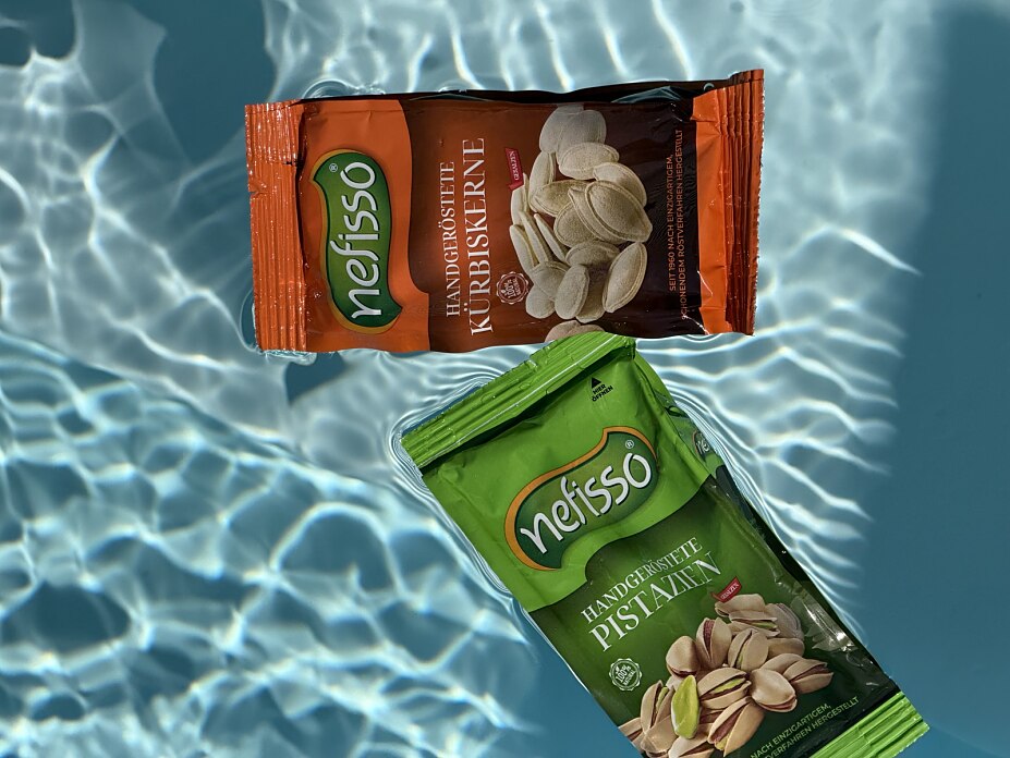 Grüne Nefisso Pistazienpackung und orange Kürbiskernpackung vor blauem Wasser